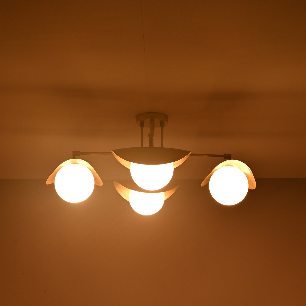 Curved brass ceiling light from Brass Leaf Studio casting indirect warm light through sculpted metal shades and opal globes.