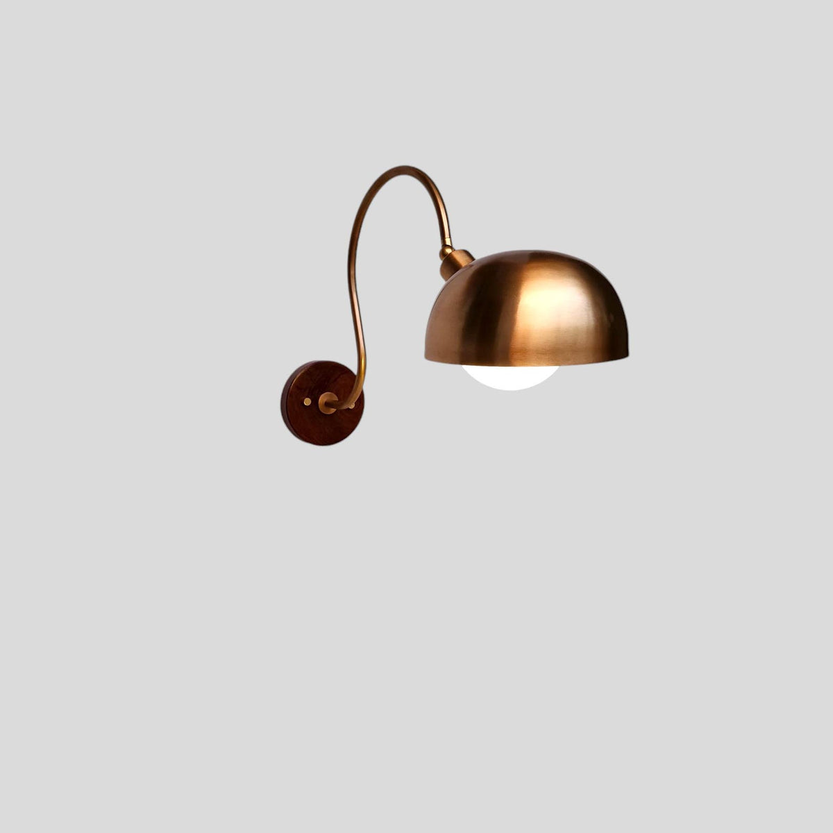 Profile view of curved arm brass wall sconce with dome shade and warm glow