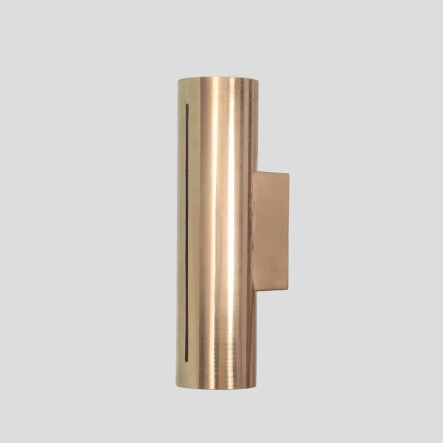 Handmade cylindrical brass wall sconce with vertical glowing slit design, crafted by Brass Leaf Studio for modern and industrial interiors.