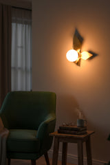Closeup of decorative brass leaf wall sconce with warm globe illumination and sculptural raw brass finish