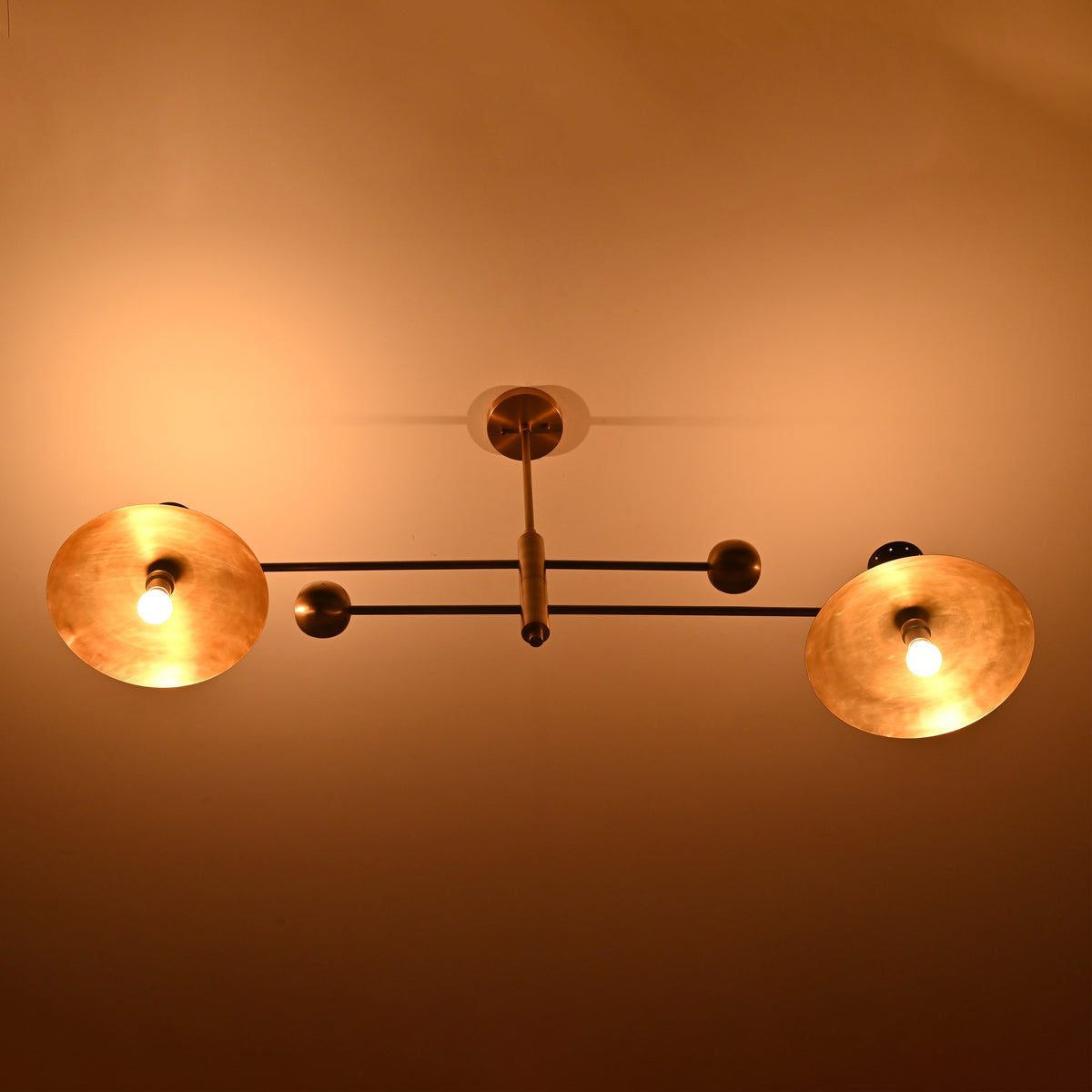 Top angle of Diabolo chandelier illuminated in warm light, highlighting brushed brass bowls and black cone accents.