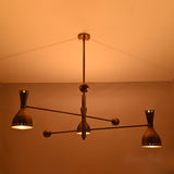 Diabolo brass chandelier illuminated in warm ambient light, creating a soft indirect glow ideal for living and dining spaces.