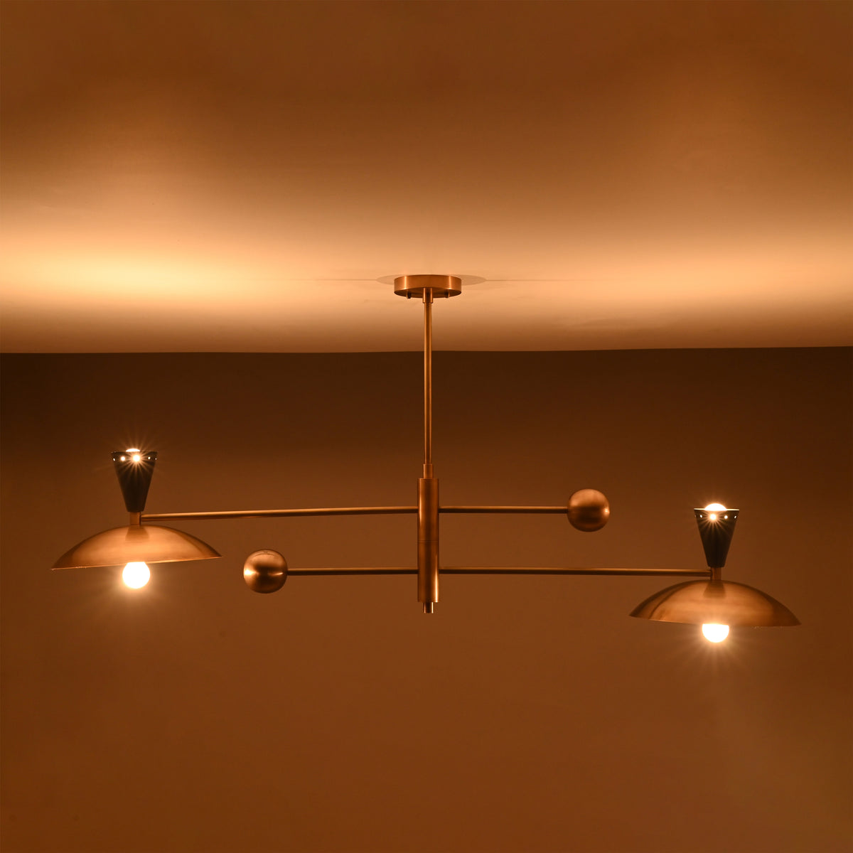 Warm-lit front view of Diabolo brass chandelier with glowing bowl-shaped shades creating soft ambient illumination.