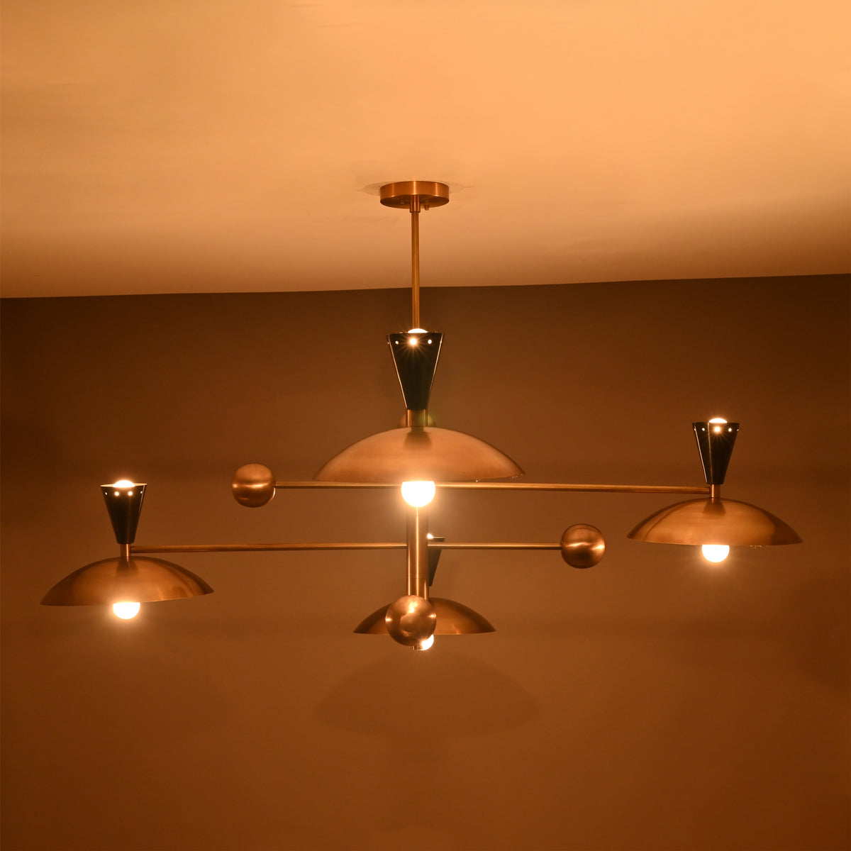 Warm-lit front view of Diabolo 8-light chandelier with brass bowl shades glowing in soft ambient lighting.