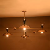 Warm-lit front view of Diabolo 8-light chandelier with brass bowl shades glowing in soft ambient lighting.
