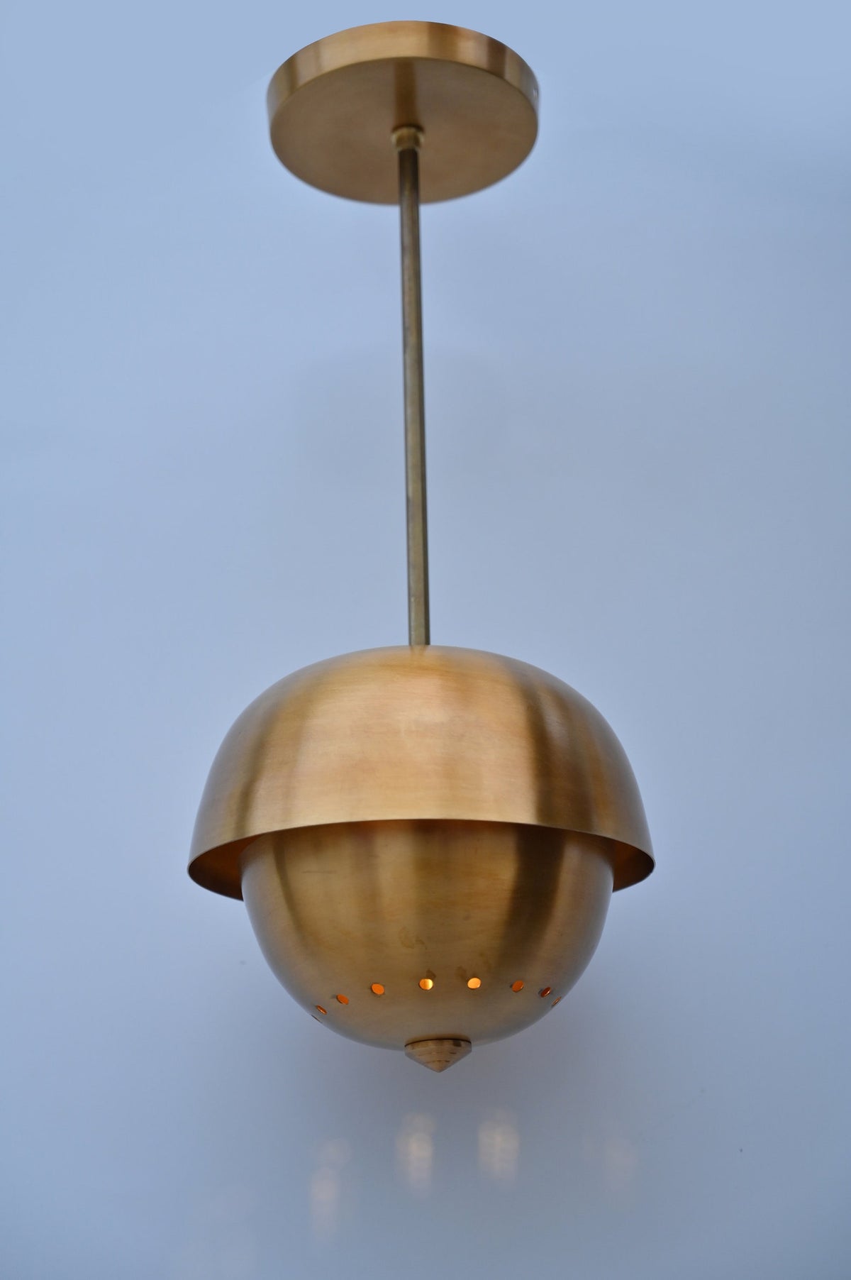 Brass dome pendant light with perforated detail at bottom glowing softly when lit