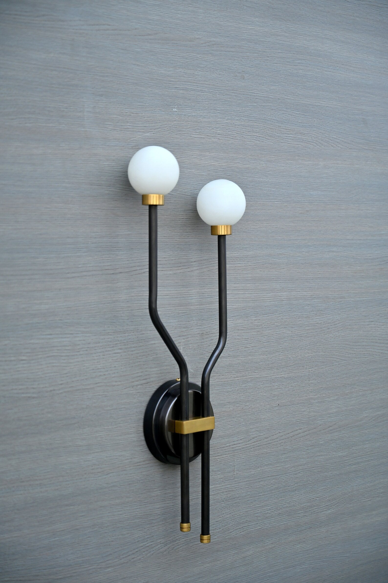 Angled close-up of handcrafted double globe wall sconce with brass accents and frosted globes