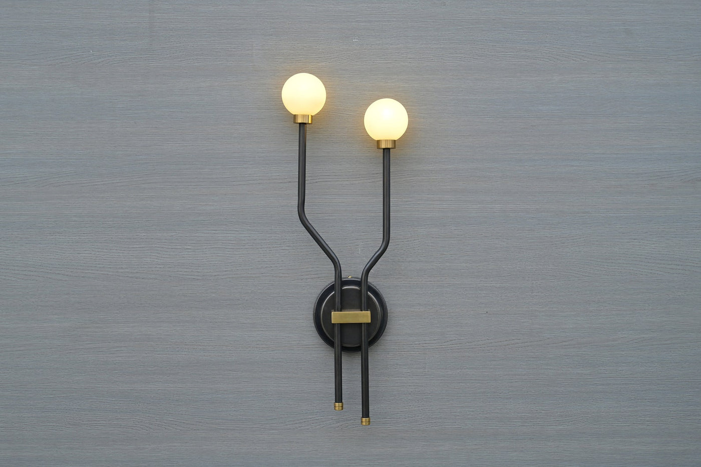Front view of double globe brass wall sconce with minimalist black frame and frosted globes