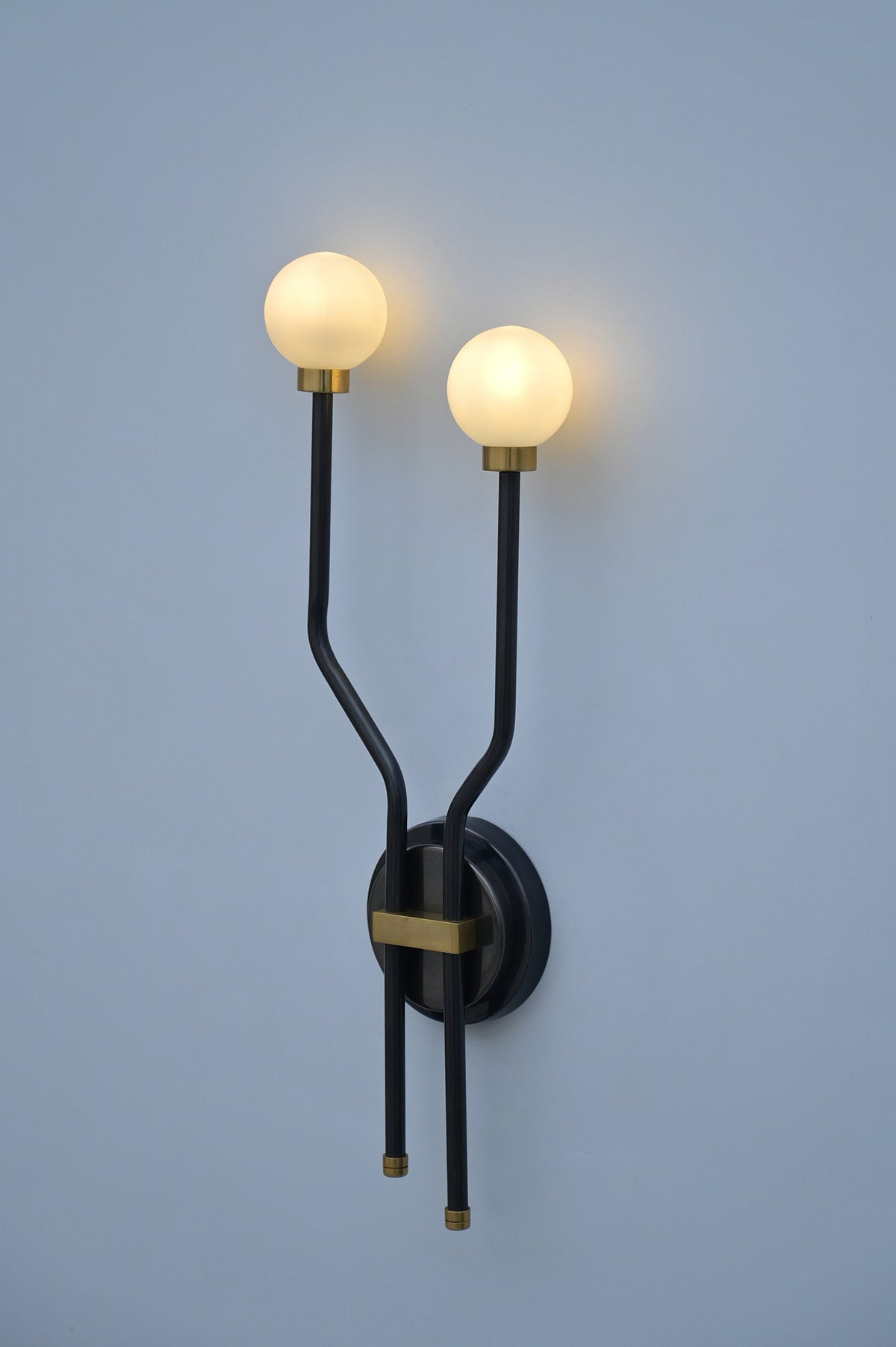 Modern double globe wall sconce in brass and black, illuminated with warm ambient lighting