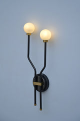 Modern double globe wall sconce in brass and black, illuminated with warm ambient lighting