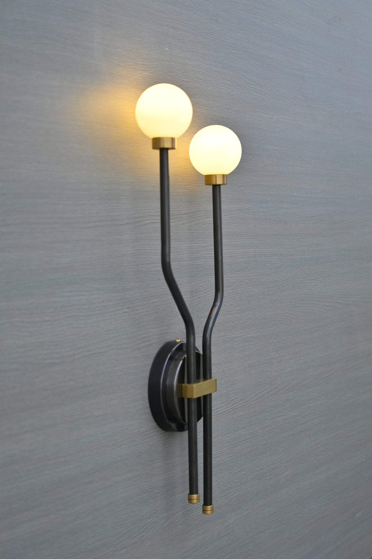 Side angle view of double globe brass wall sconce with glowing frosted glass globes