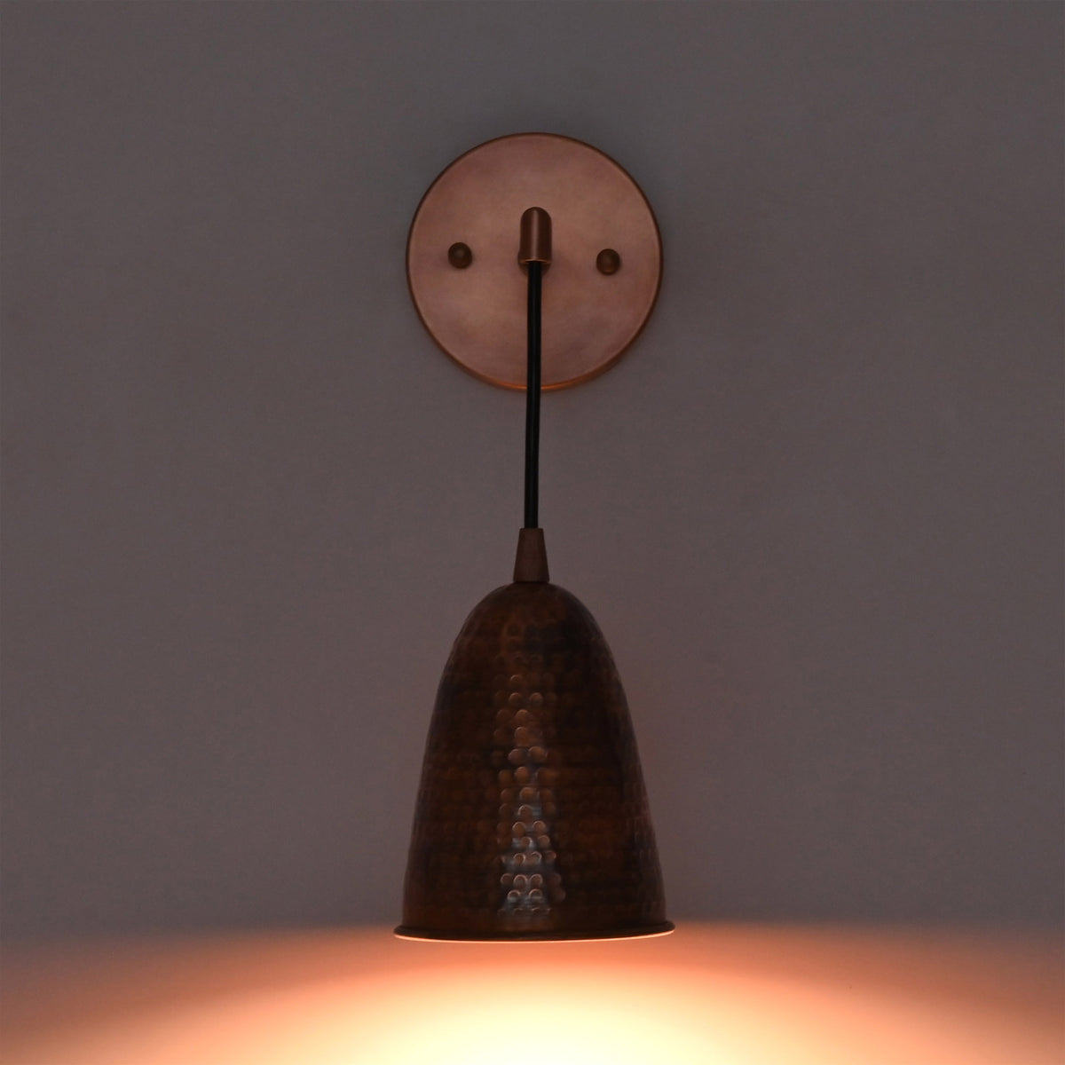 Front view of the Hudson Modern Hammered Copper Cone Wall Sconce mounted on a wall with warm downward illumination, showcasing the handcrafted hammered copper cone shade and minimalist design.