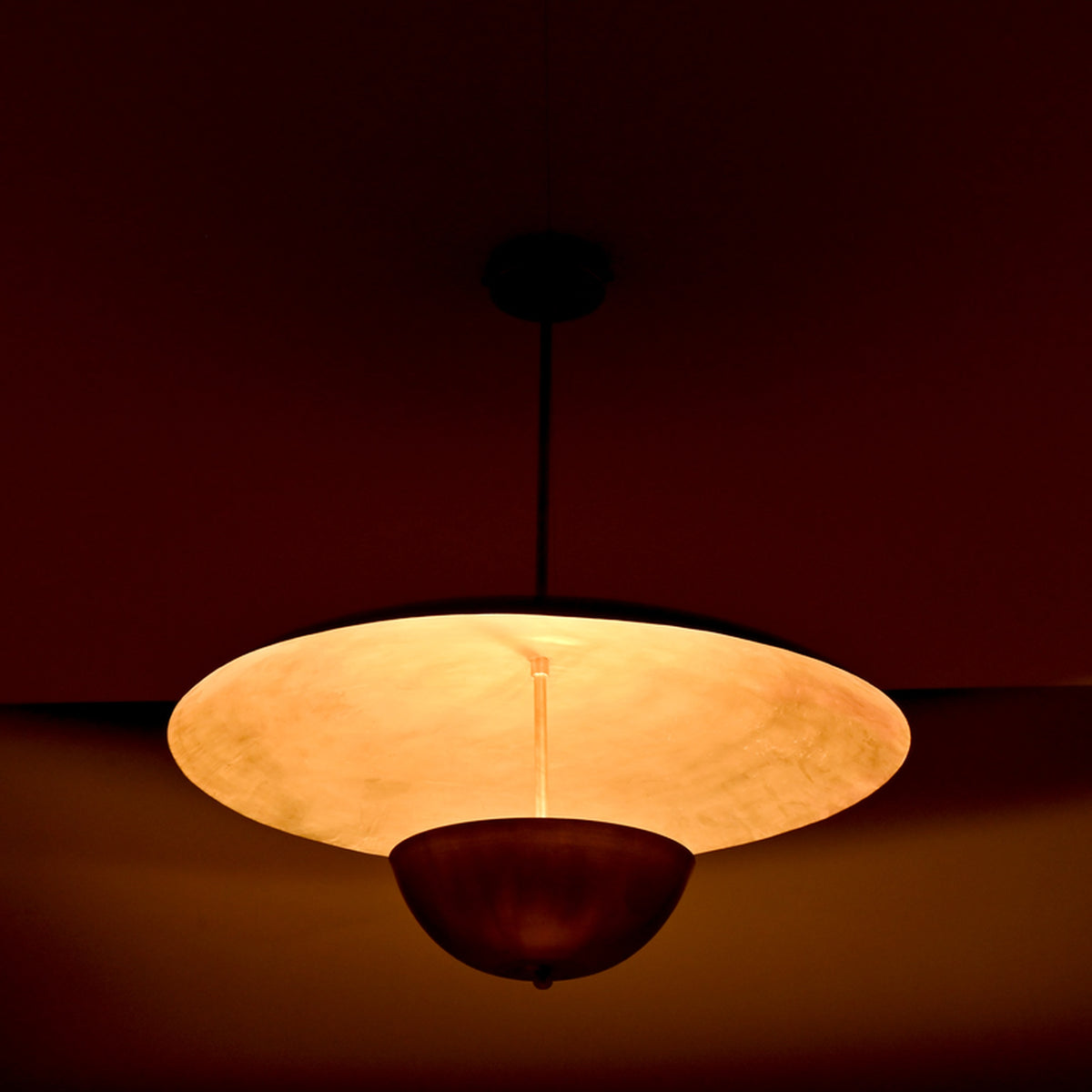 Close-up night view of brass dual-shade pendant highlighting the warm inner glow and reflective brass surfaces.