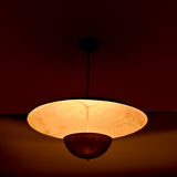 Close-up night view of brass dual-shade pendant highlighting the warm inner glow and reflective brass surfaces.