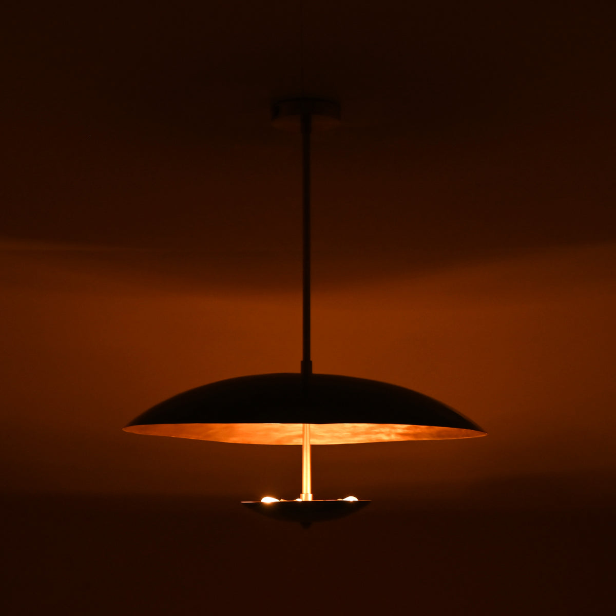 Handcrafted emerald green brass pendant light at night illuminating space with rich warm brass glow