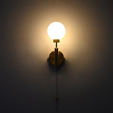 Pull chain globe wall sconce in raw brass finish, illuminated with a warm glow from the frosted glass globe shade.