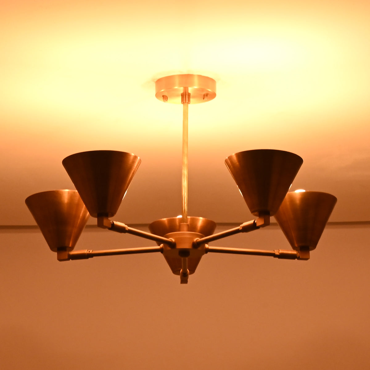 Bottom view of five-light brass cone chandelier highlighting warm indirect lighting and symmetrical arm layout.