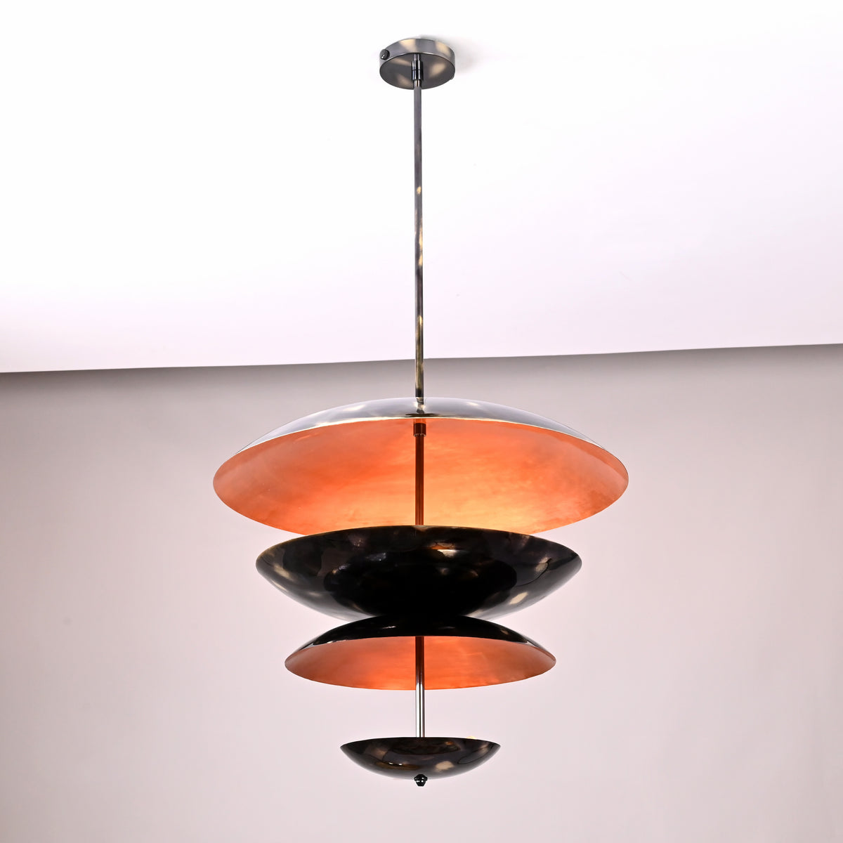 Side view of tiered disc chandelier with black brass outer and warm copper patina interior