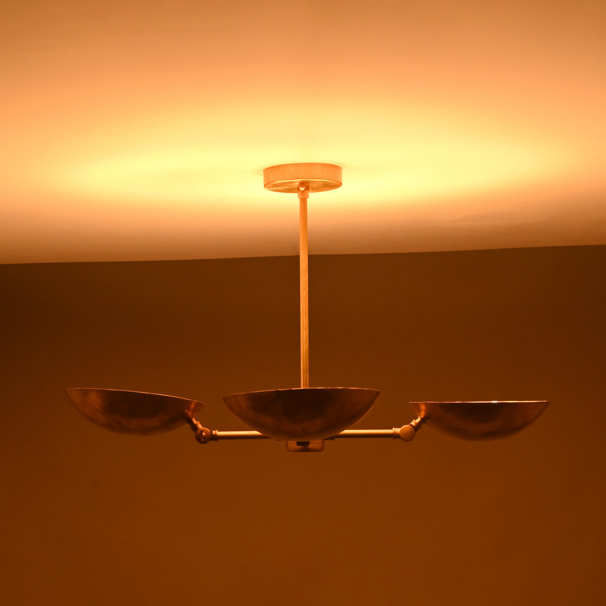 Four-bowl brass chandelier photographed in low lighting, showing deep golden glow and atmospheric ceiling illumination.