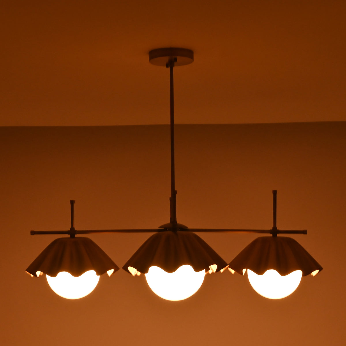 Bottom view of four-light brass chandelier showcasing warm indirect lighting and scalloped shade edges.