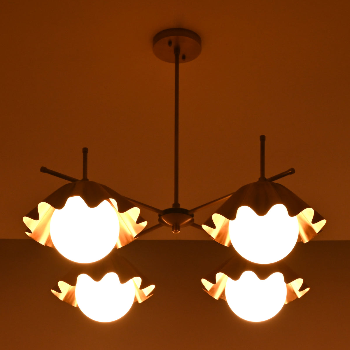 Top view of four-light brass chandelier glowing warmly with sculpted bowl-shaped shades.