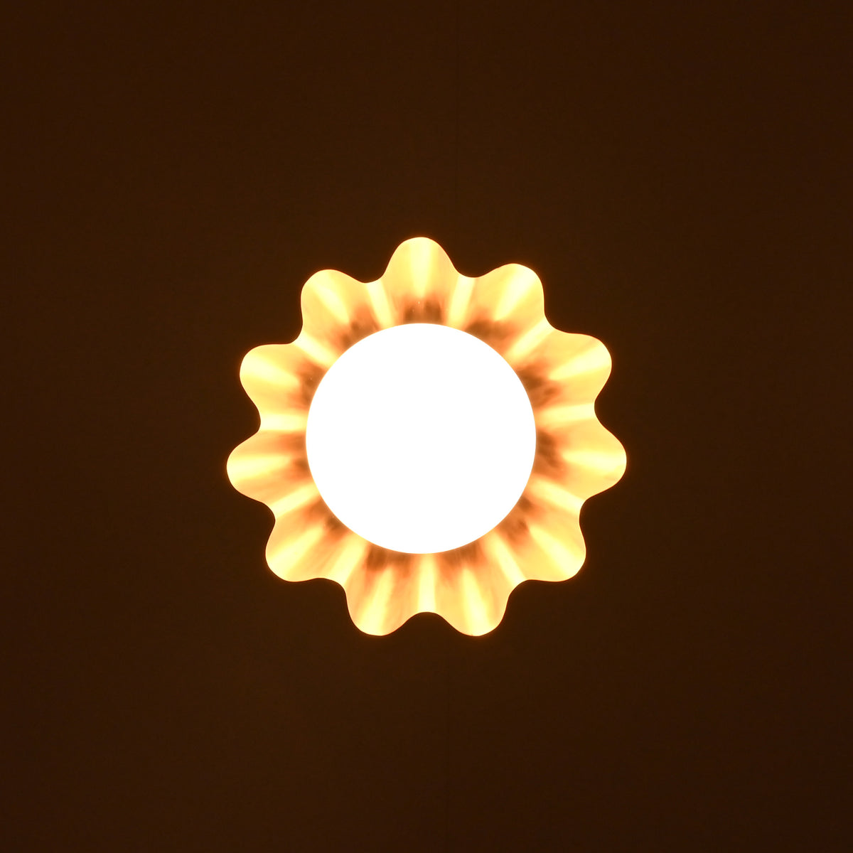 Bottom glowing view of brass pendant lamp with ruffled shade and globe bulb casting ambient light