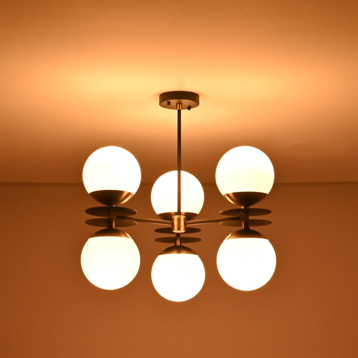 Brass and black chandelier with six opal glass globes glowing warmly against the ceiling