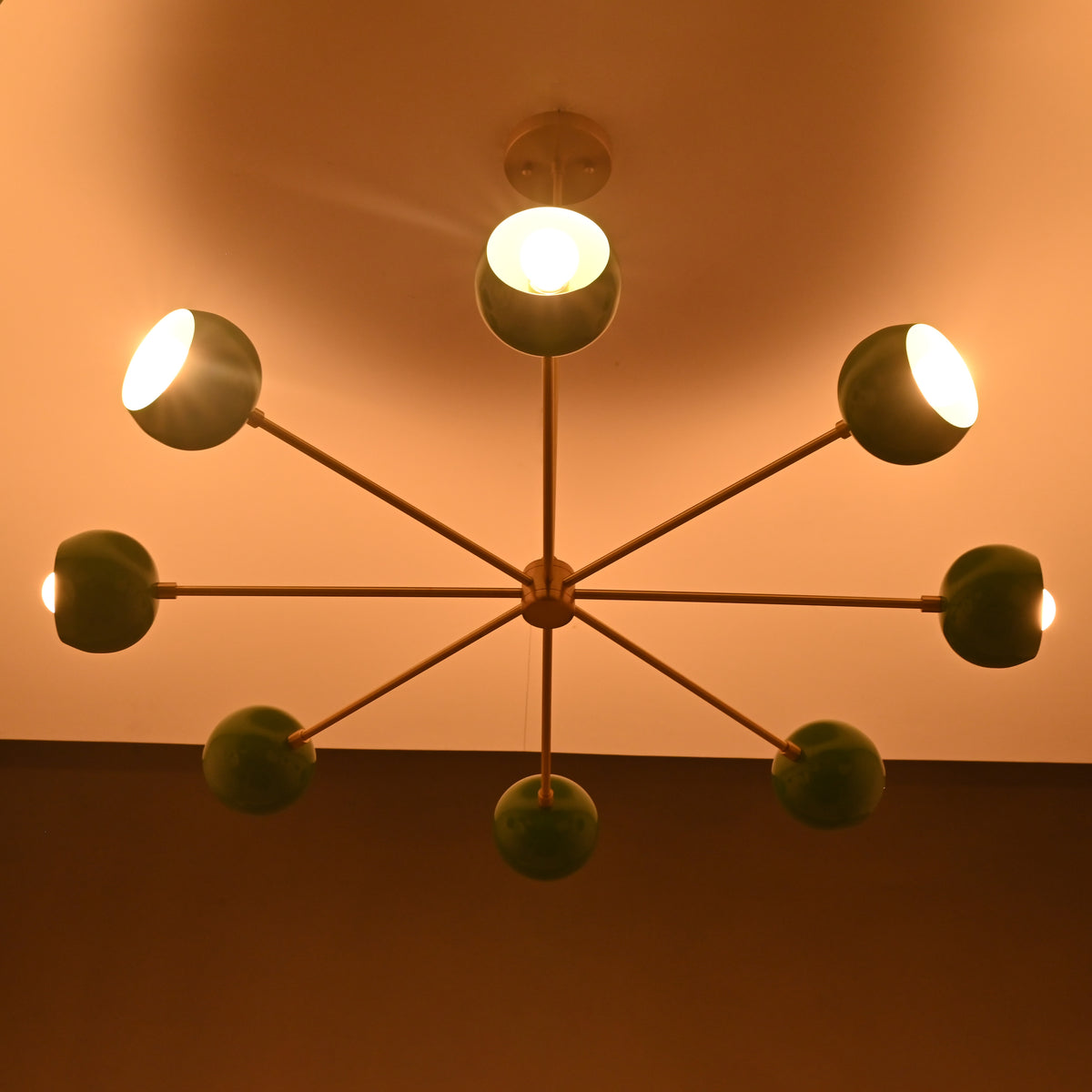 Green bowl sputnik chandelier casting warm indirect light across ceiling with soft modern ambiance