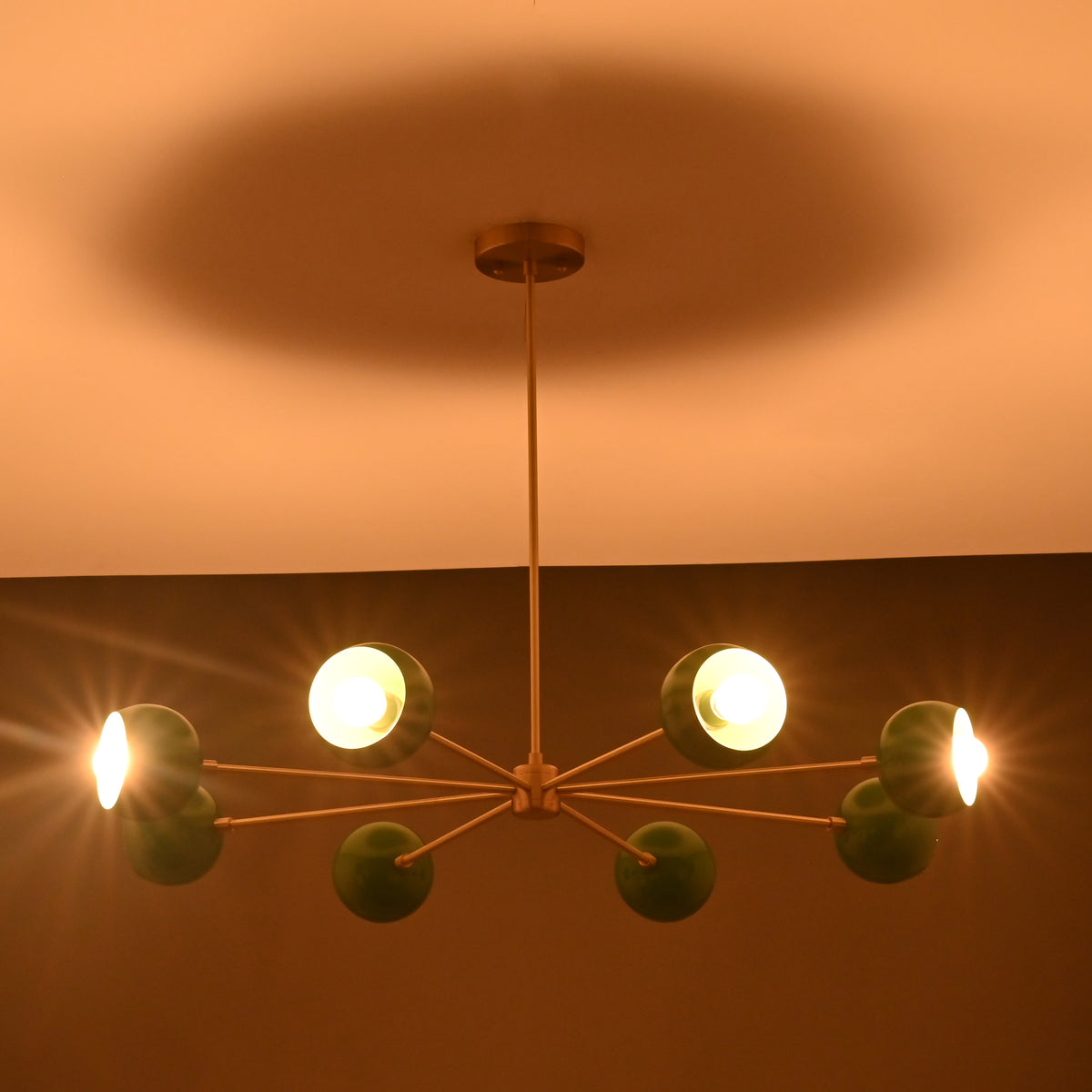 Close-up of green enamel chandelier lit against warm ceiling tone