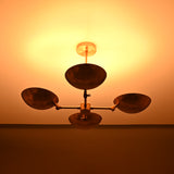Wide view of brass bowl chandelier illuminated in a dark room, casting soft ambient glow and showcasing handcrafted hammered brass shades.