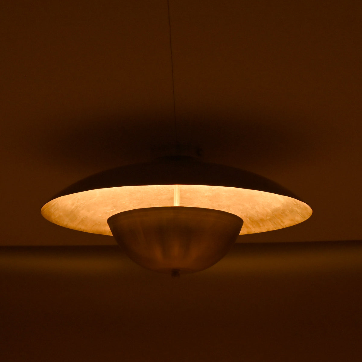 Handcrafted brass disc light with soft inner glow highlighting its smooth circular form in a dimly lit room