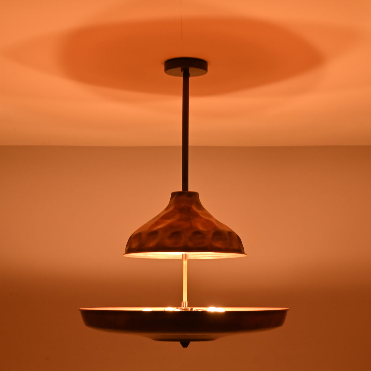 Handcrafted copper disc chandelier enhancing warm interior ambience with indirect brass lighting