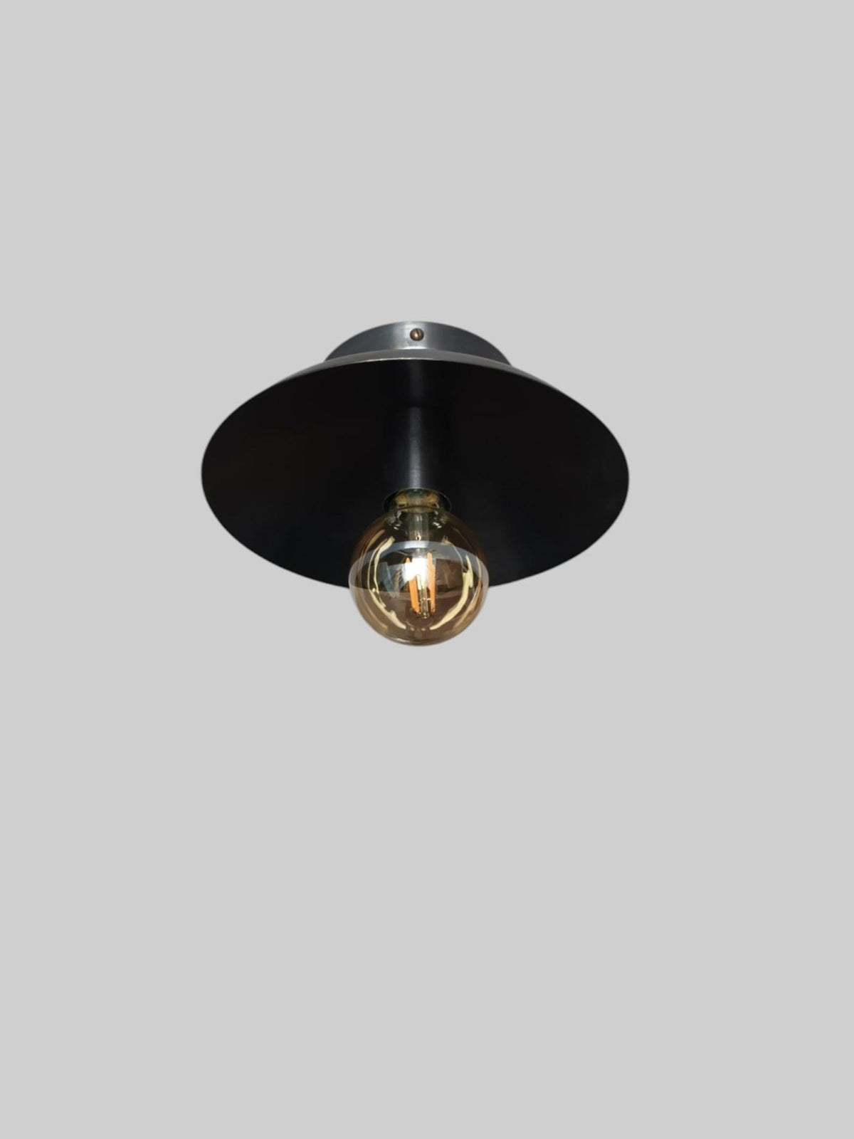 Front view of handmade blackened brass flush mount lamp with smooth dome shade and visible bulb for ambient lighting.