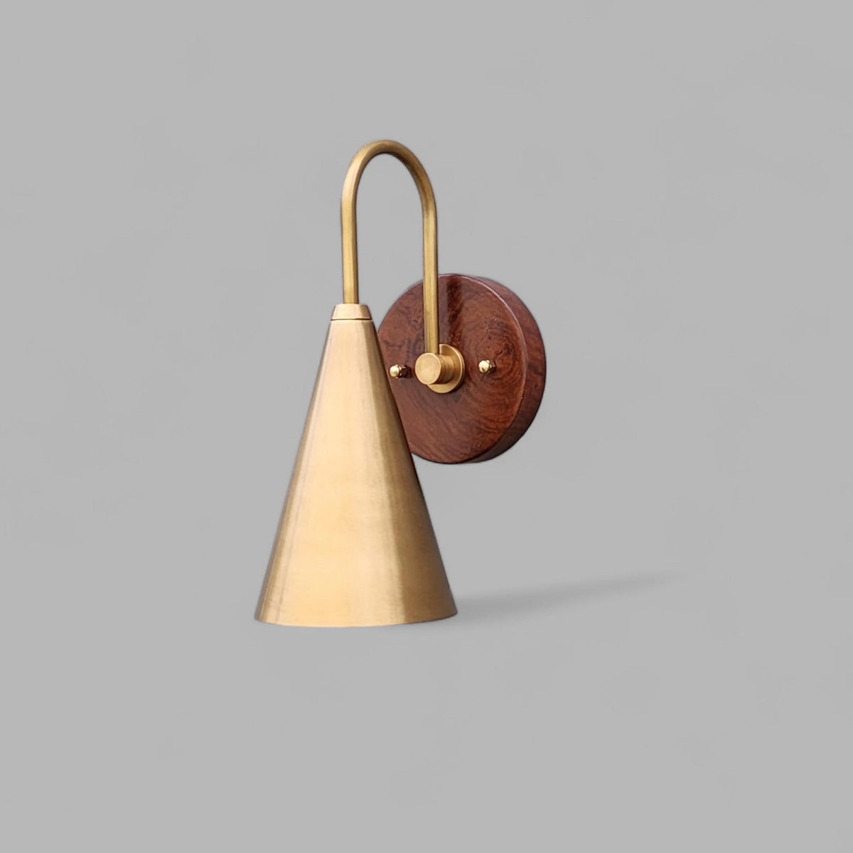 Front view of handmade brass and wood cone wall light with elegant arched arm and circular wooden wall plate.