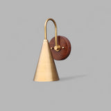 Front view of handmade brass and wood cone wall light with elegant arched arm and circular wooden wall plate.