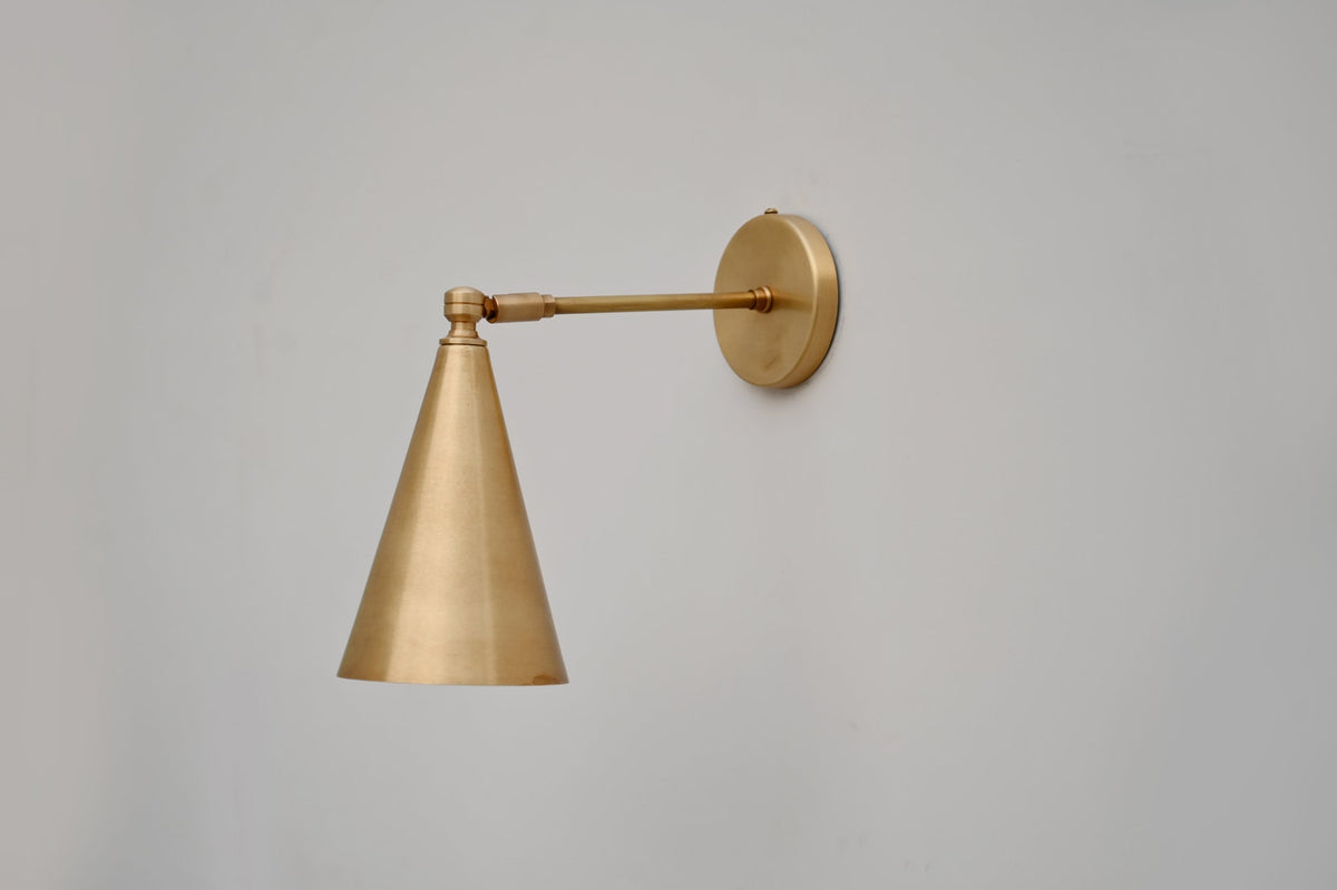 Handmade brass cone wall light with sleek linear arm and round wall mount, ideal for bedrooms and reading spaces.