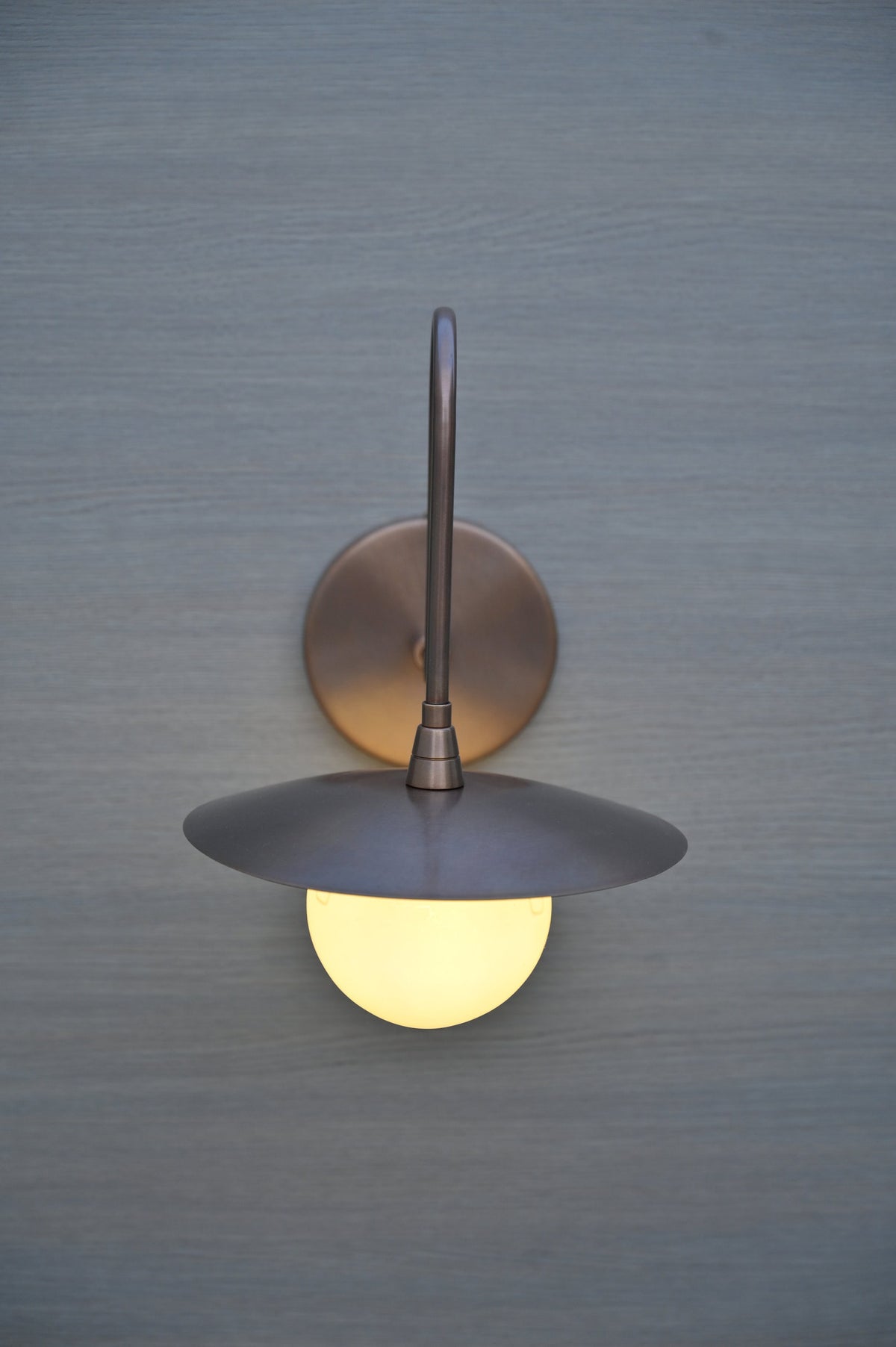 Front view of handmade brass wall sconce with globe glass shade and flat bowl cover, mounted on wall.