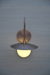Front view of handmade brass wall sconce with globe glass shade and flat bowl cover, mounted on wall.