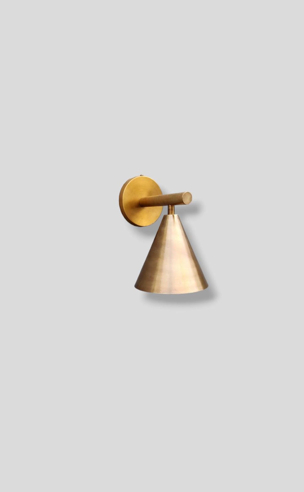 Angled perspective of handmade brass cone wall sconce showing sleek conical shade and solid brass build for modern interiors.