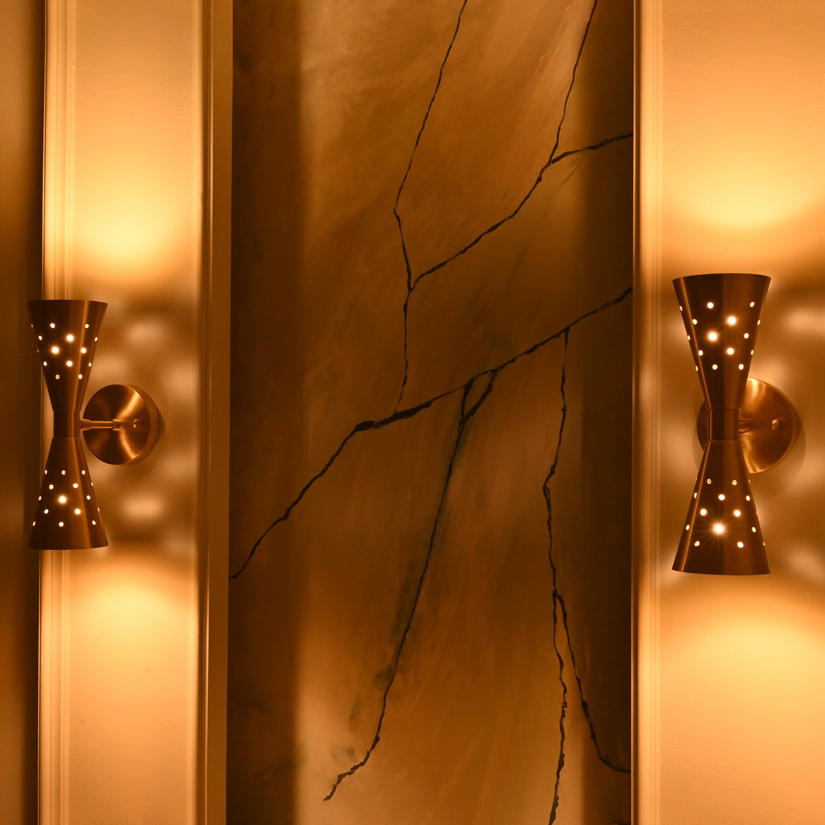 Ibiza brass wall sconces installed beside a marble feature wall with soft decorative up and down lighting