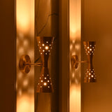 Mid century inspired brass wall sconce with hourglass silhouette, perforated details and warm ambient glow