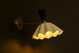Handcrafted brass wall sconce with flared fluted shade illuminated at night creating warm soft ambient glow