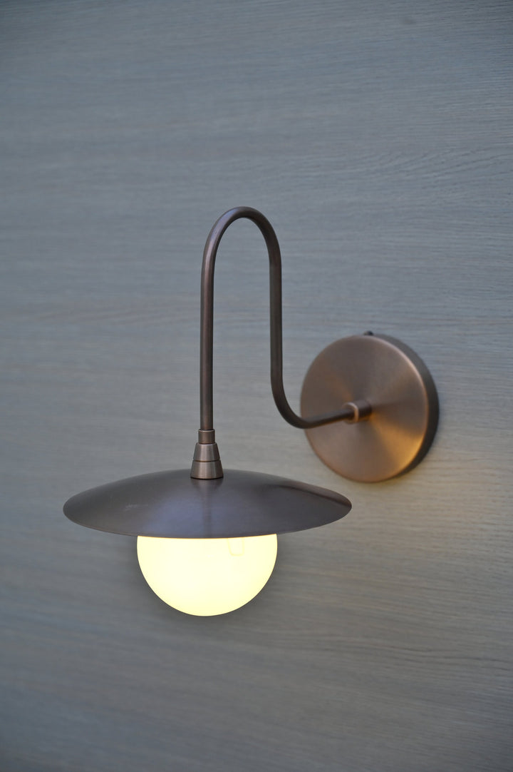 Side view of industrial brass wall sconce with matte finish, curved arm, and glowing glass globe shade.