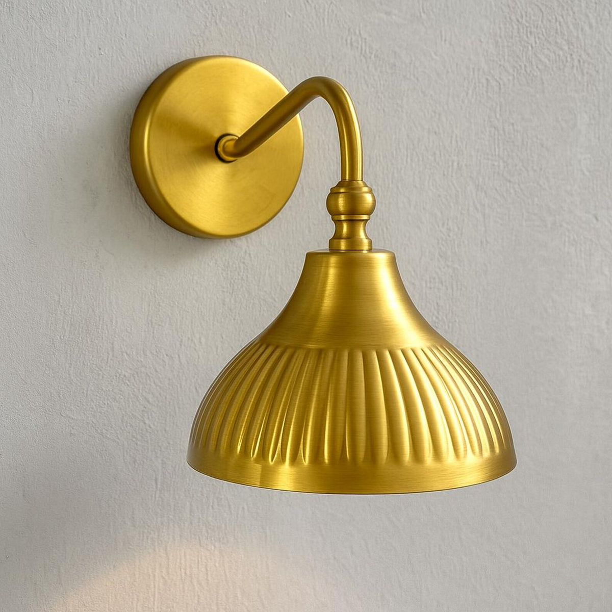 Industrial style brass wall sconce with ribbed dome shade mounted on light textured wall surface.