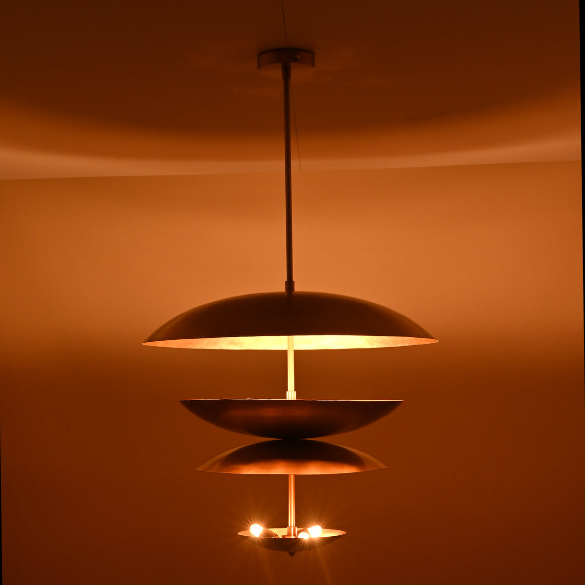Full view of illuminated layered brass 6-light chandelier with floating disc-shaped shades and warm glow.
