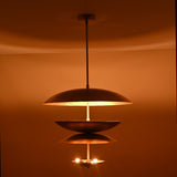 Full view of illuminated layered brass 6-light chandelier with floating disc-shaped shades and warm glow.
