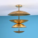 Brass flushmount chandelier with layered bowl-shaped shades against a blue wall background.