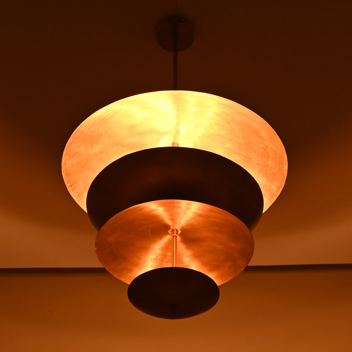 Warm-lit bottom angle of layered brass chandelier featuring stacked sculptural disc shades.
