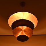 Warm-lit bottom angle of layered brass chandelier featuring stacked sculptural disc shades.