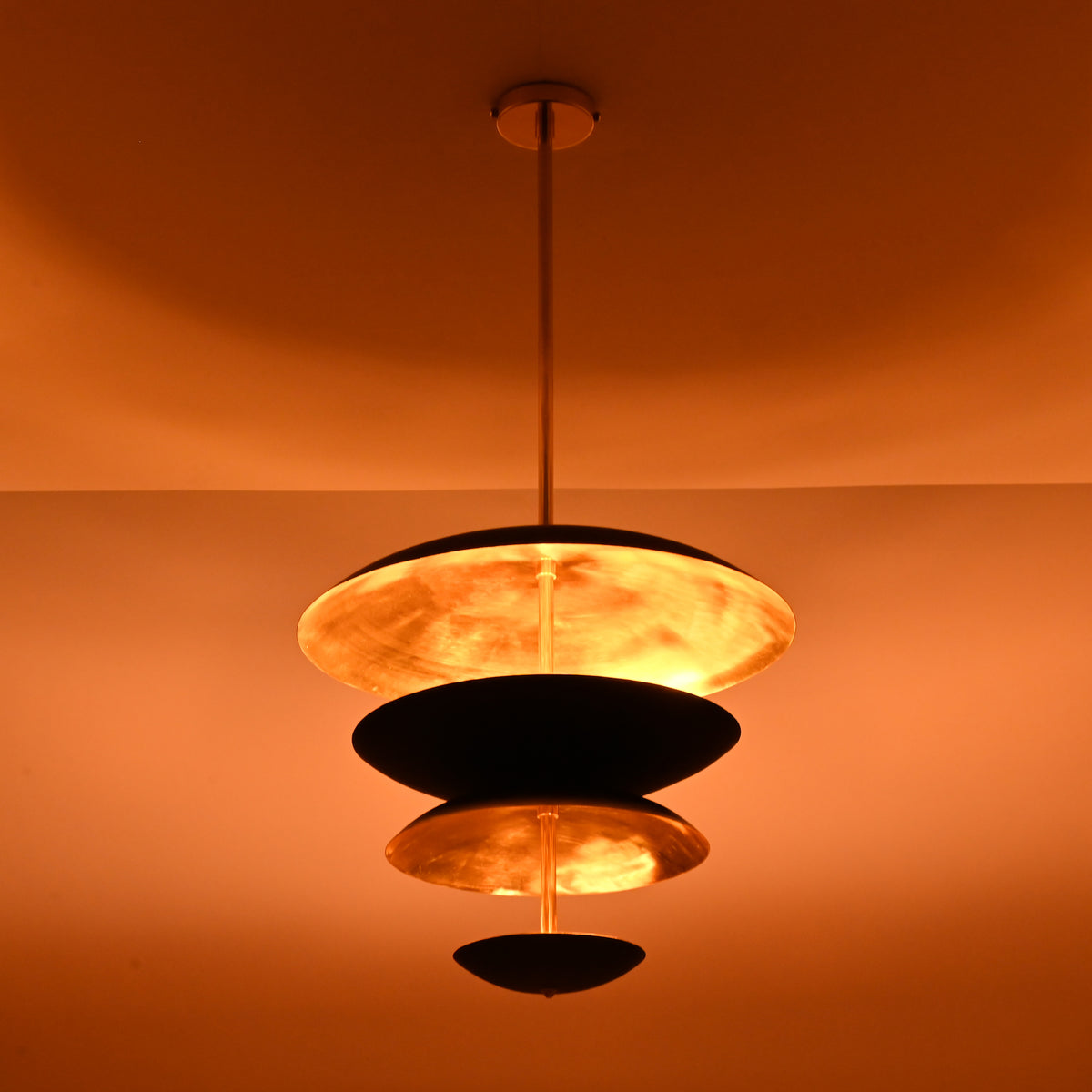 Layered brass and black disc chandelier emitting soft ambient glow, ideal for dining rooms and living spaces